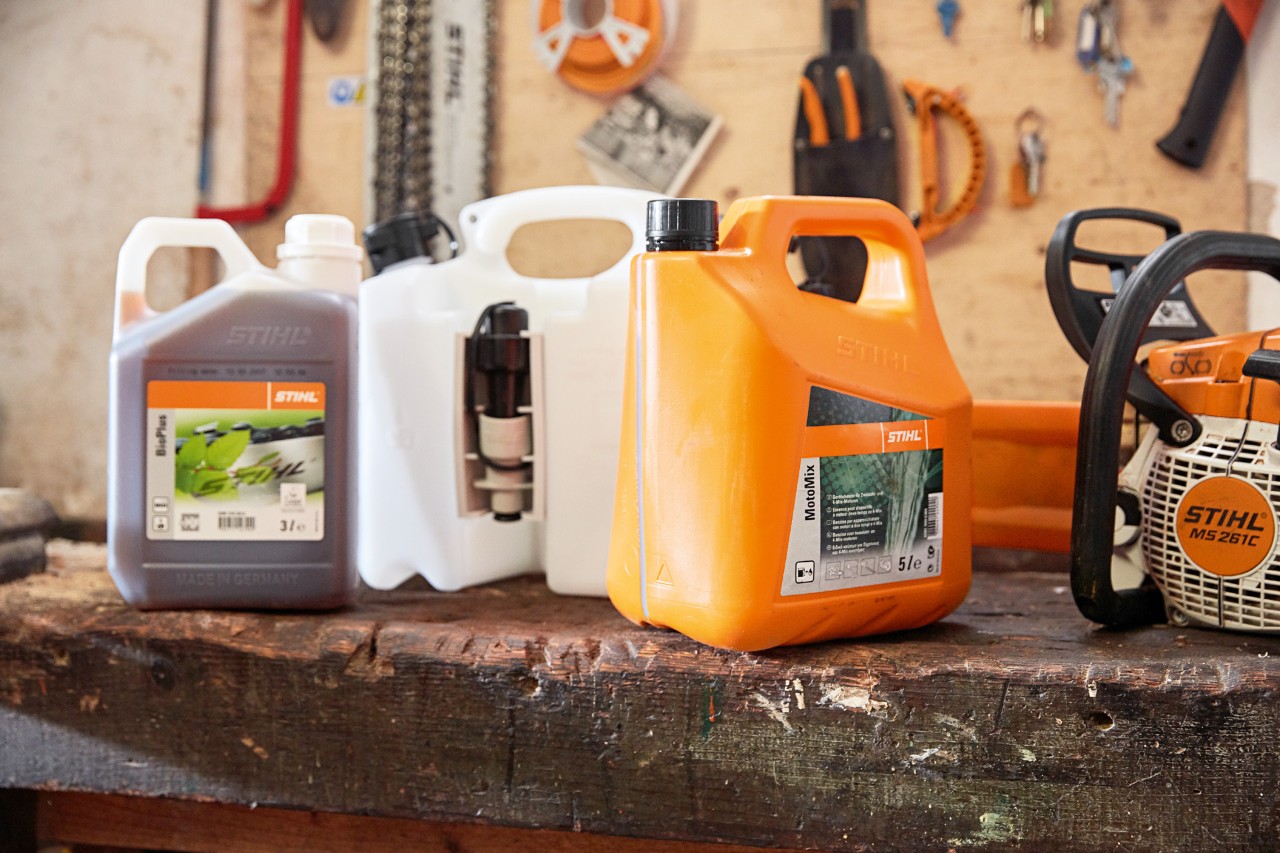 Canister with STIHL MotoMix chainsaw mixture, oil and petrol and a STIHL MS 261 C petrol chainsaw in a workshop