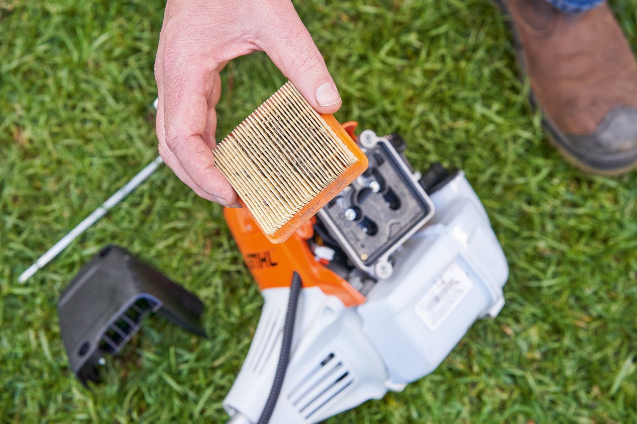 A person removing the air filter from a STIHL brushcutter to clean it 