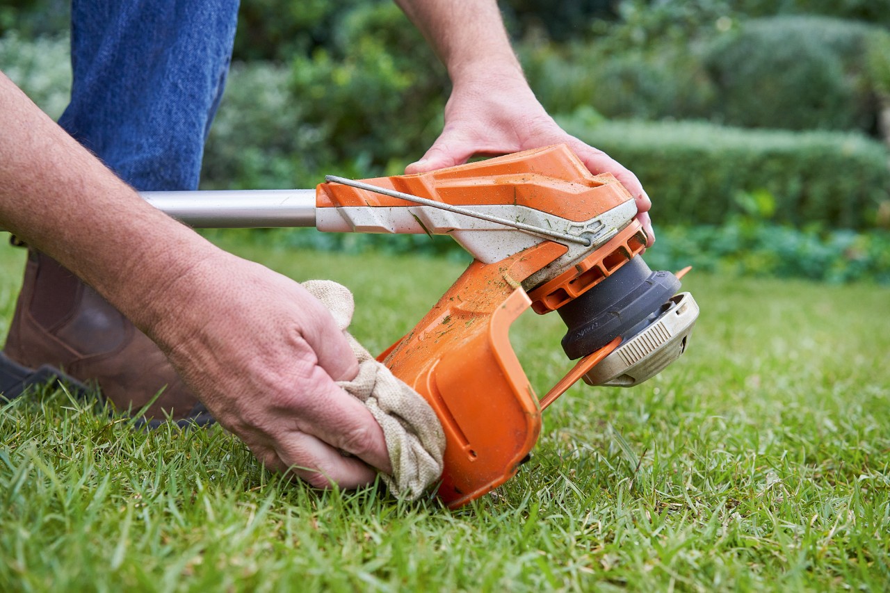 A person cleaning the guard of a STIHL brushcutter with a damp cloth