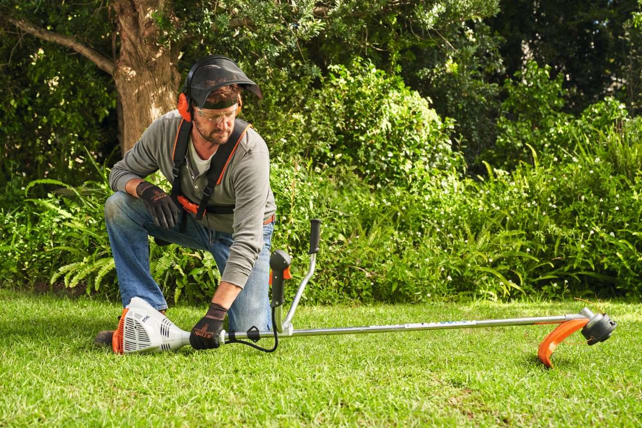 A man placing a STIHL FS 56 petrol brushcutter on the ground to start it