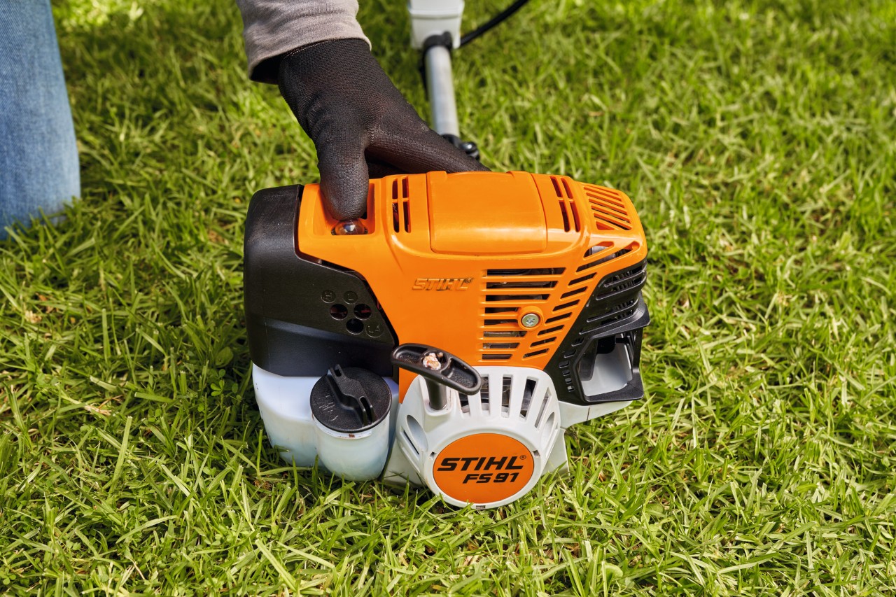 A man pressing the fuel pump of a STIHL FS 91 petrol brushcutter to start it