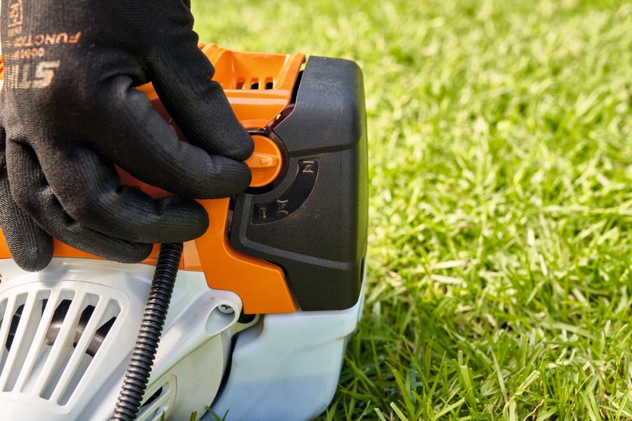 A man adjusting the fuel pump lever of a STIHL FS 91 petrol brushcutter to start it