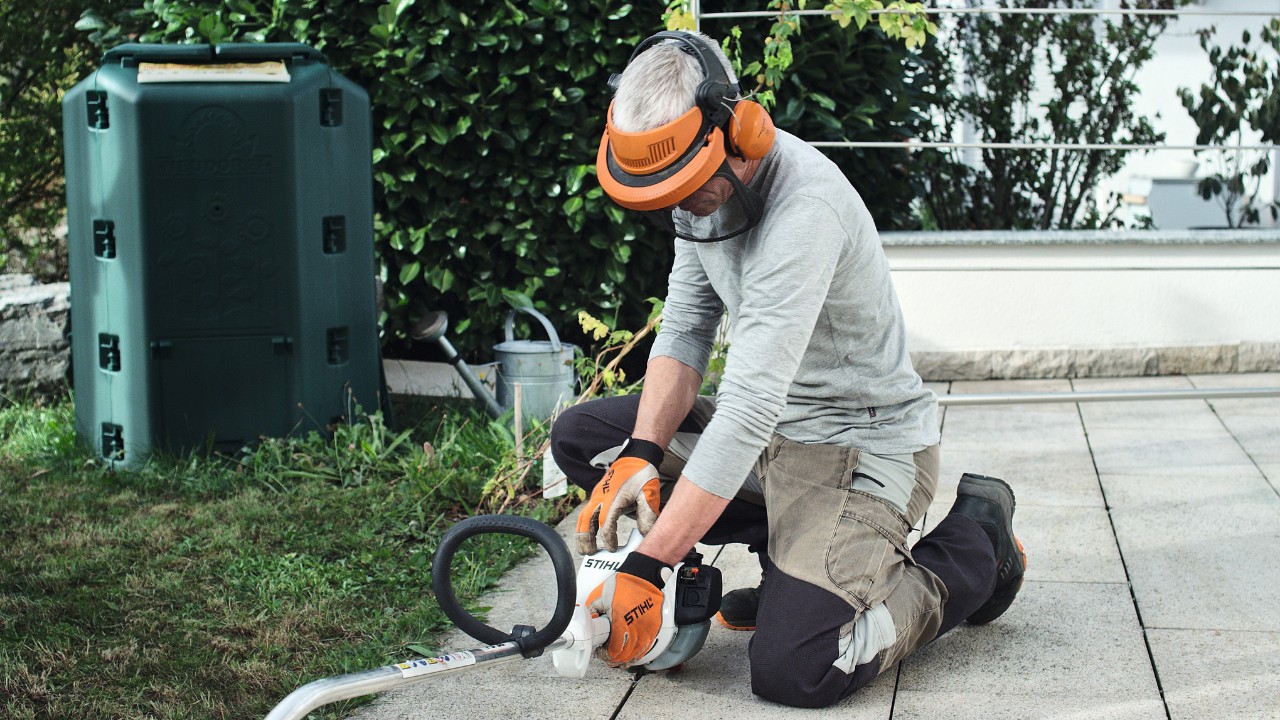 A STIHL FS 38 petrol brushcutter being pressed onto the ground by a person wearing protective clothing