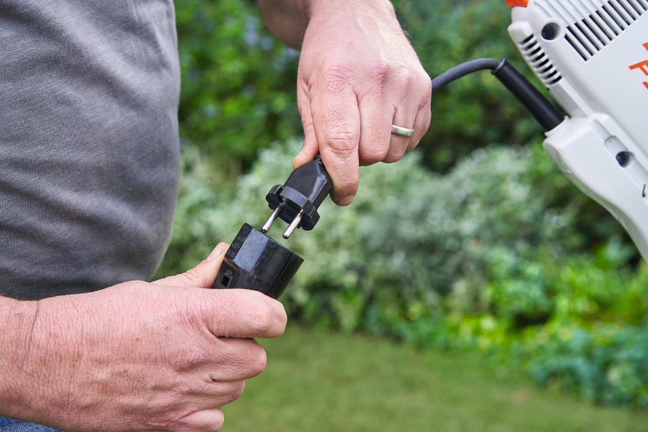 A man wearing protective gloves actuating the trigger of the STIHL FSE 60 electric brushcutter to start it