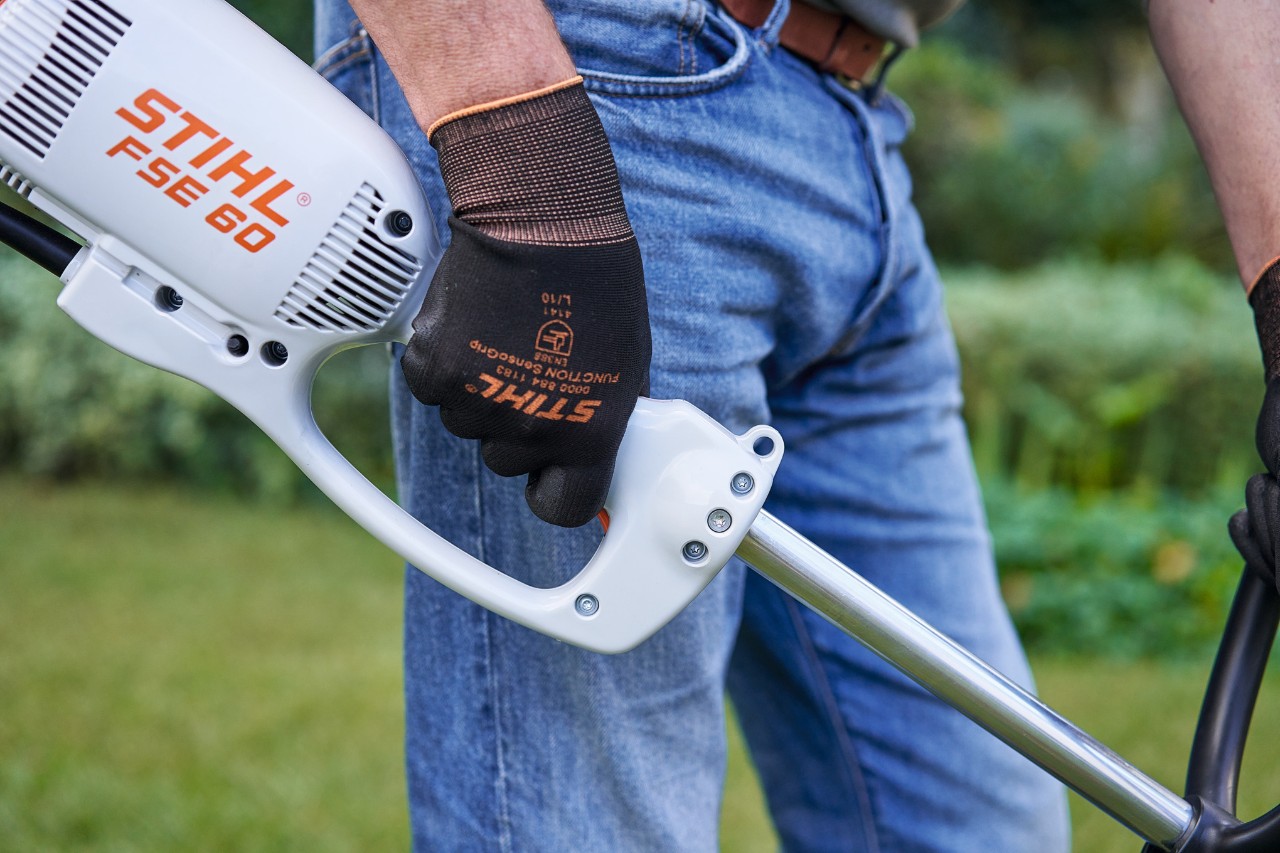 Man pressing the switch on the control handle of a STIHL FSE 60 electric brushcutter
