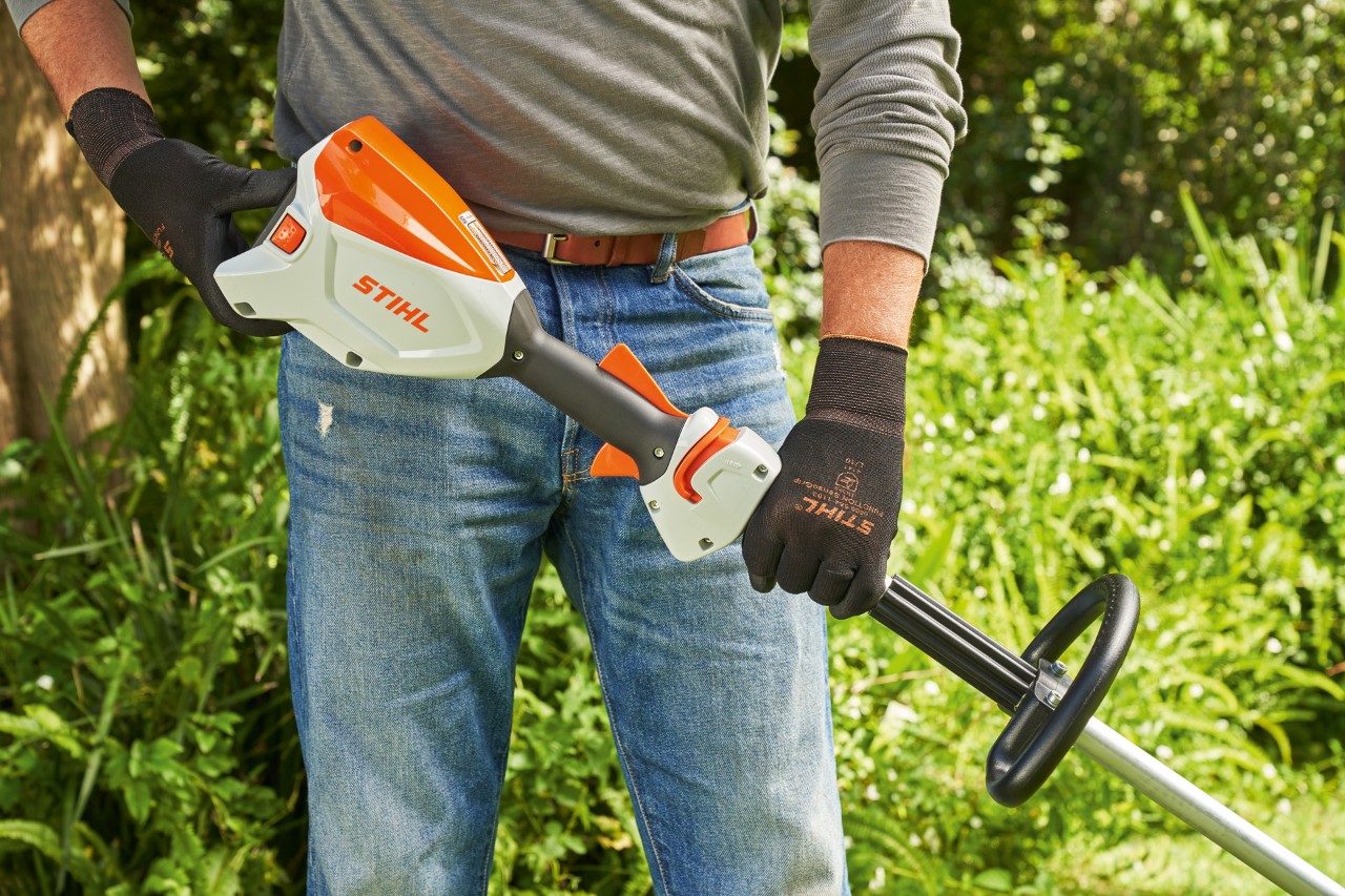 Man wearing protective gloves checking the battery of the STIHL FSA 60 cordless brushcutter before starting the brushcutter