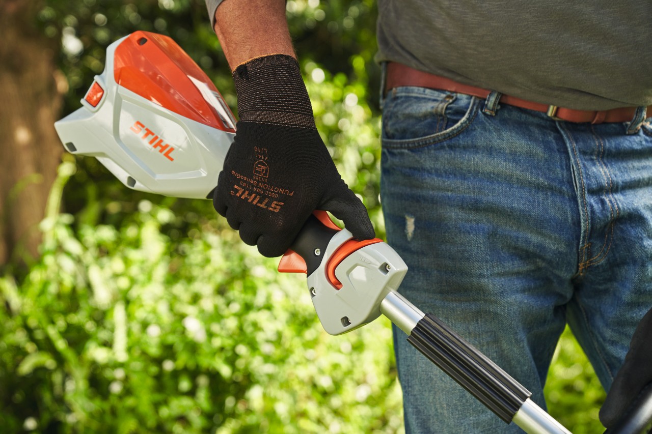 Man wearing protective gloves pushing the release slide of the STIHL FSA 60 cordless brushcutter towards the loop handle