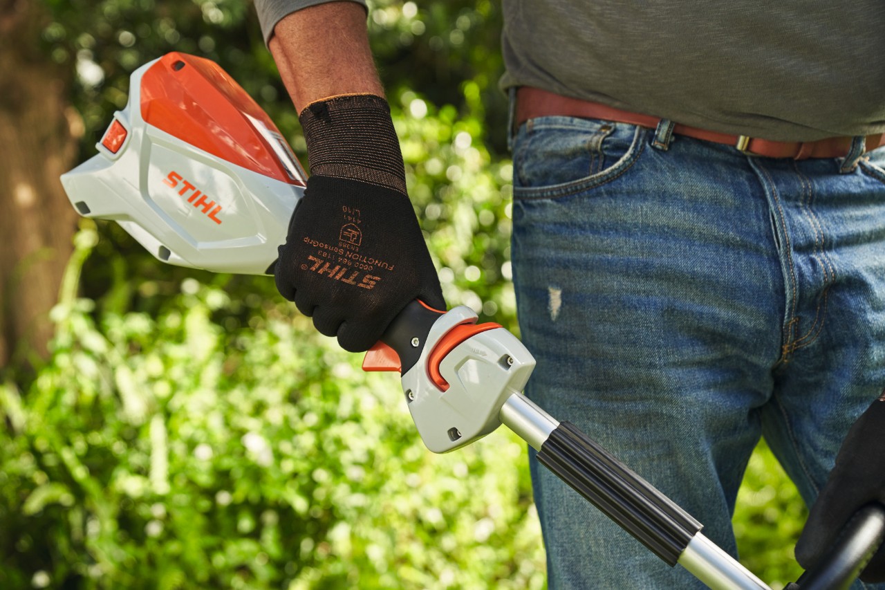 A man wearing protective gloves pressing the trigger lock on a STIHL FSA 60 cordless brushcutter 