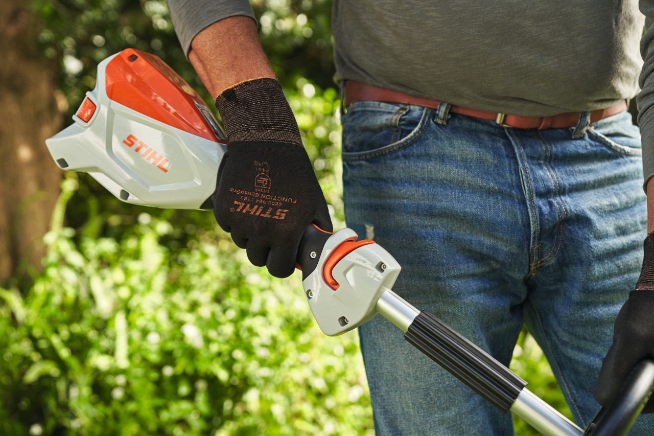Man wearing protective gloves pressing the trigger of the STIHL FSA 60 cordless brushcutter to start it