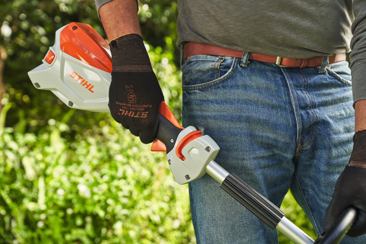 A man wearing protective gloves releasing the trigger of the STIHL FSA 60 cordless brushcutter to switch it off