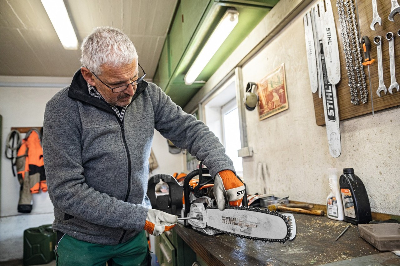 A man in a workshop screwing a STIHL Rollomatic E guide bar onto a chainsaw 