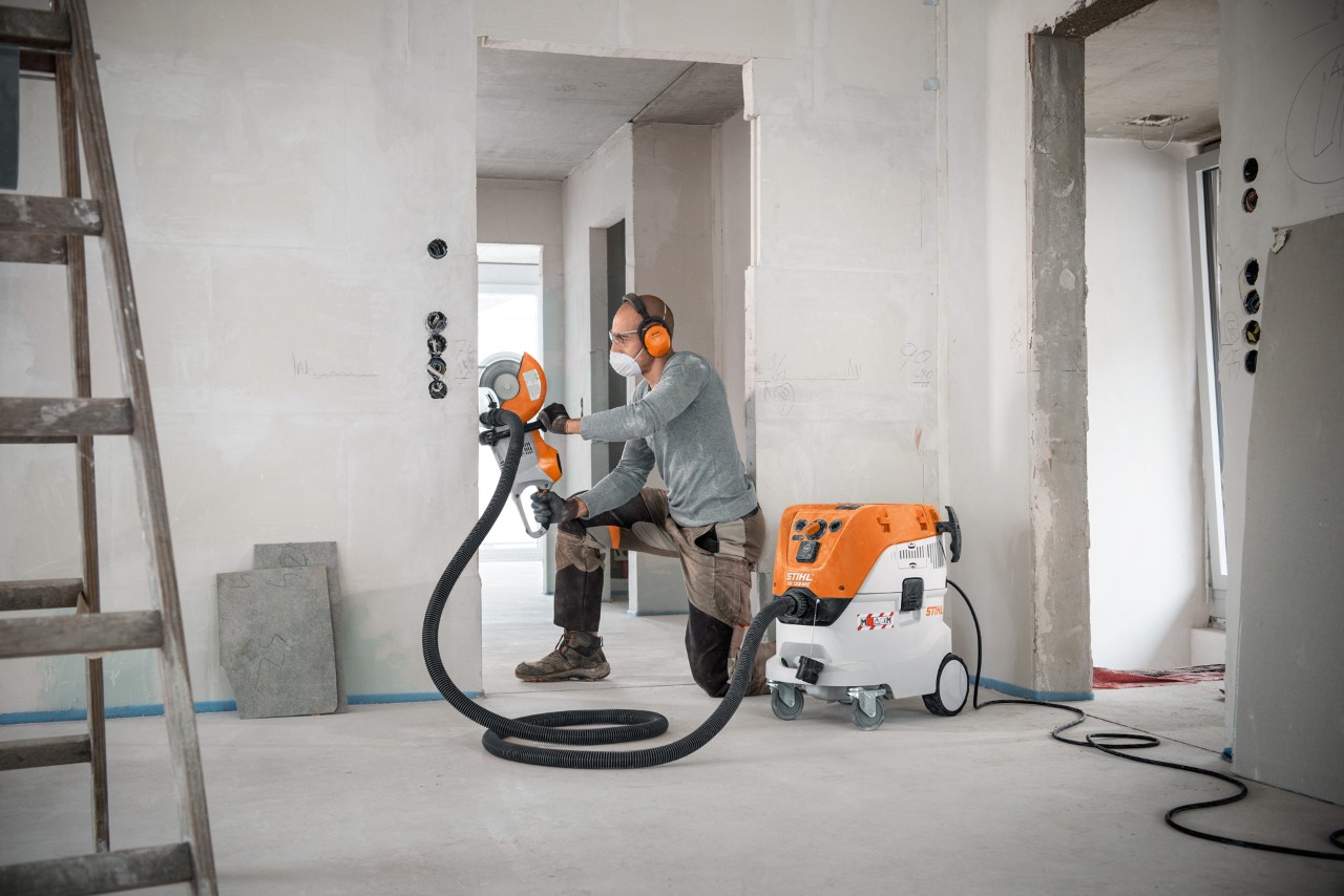 A man using a STIHL SE 133 ME wet and dry vacuum cleaner while working with a STIHL TSA 230 cut-off machine
