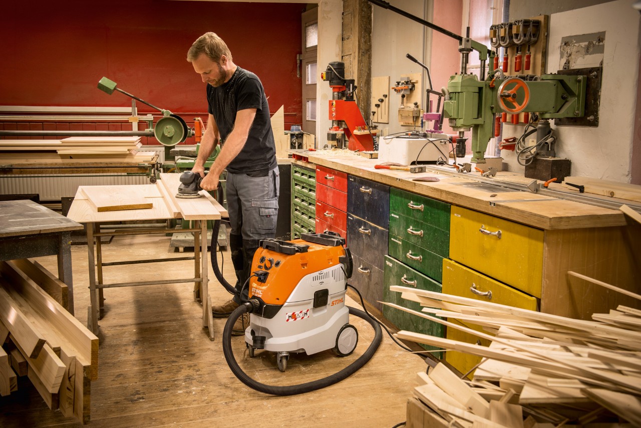 Man using a STIHL SE 133 ME wet and dry vacuum cleaner in a workshop while working with planks of wood