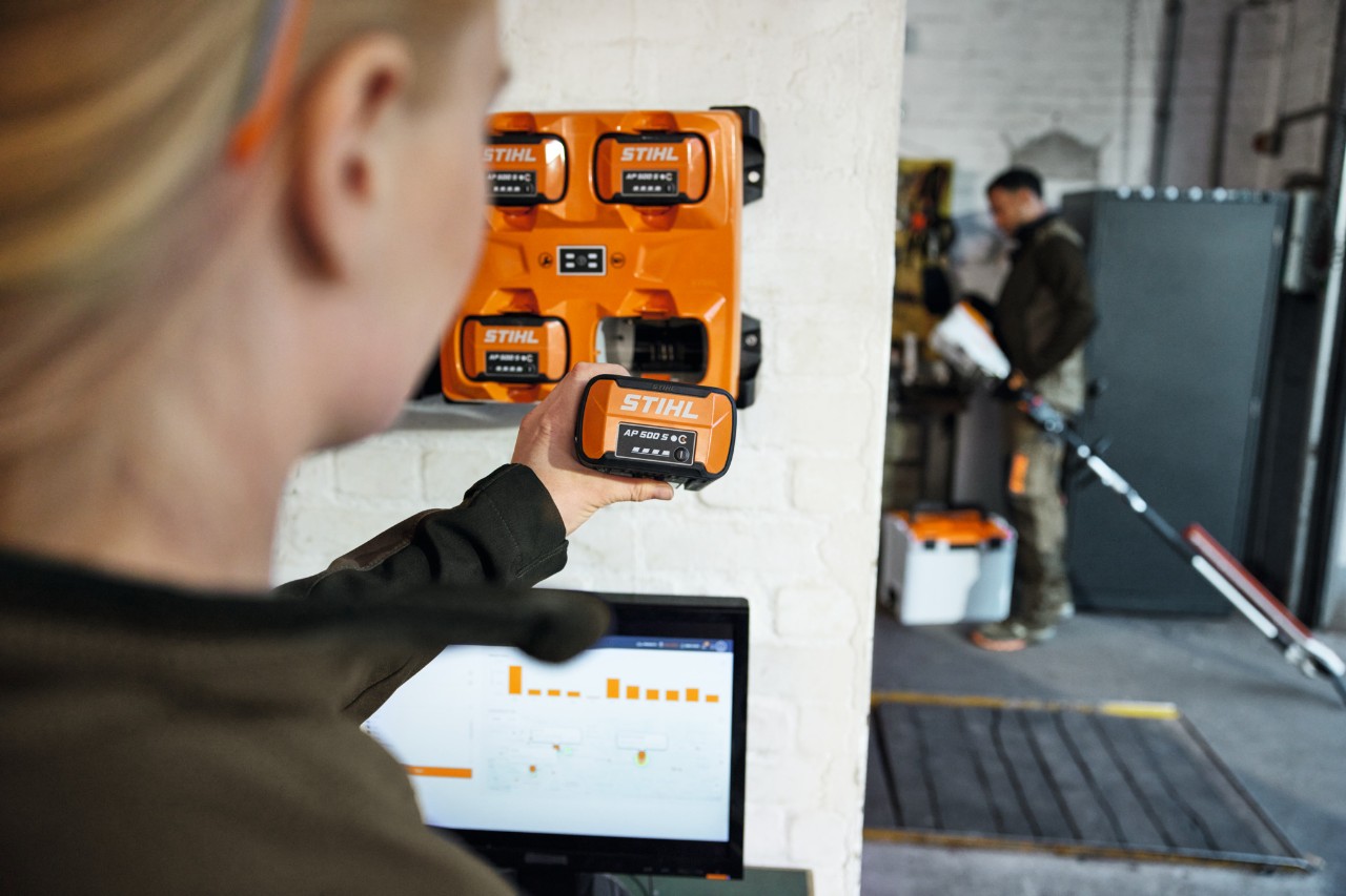 A woman in front of a laptop removing an AP 300 S from a STIHL AL 301-4 multi-charger