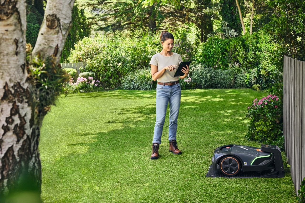 A woman operating the STIHL iMOW® EVO in her garden using a tablet