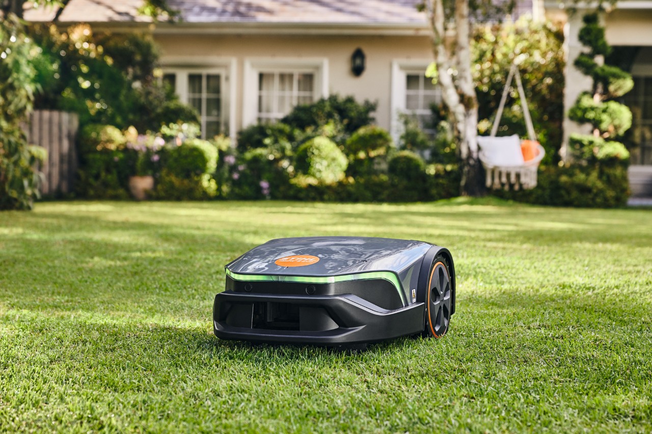 An iMOW® Evo mowing a well-maintained garden lawn in front of a house and a hammock.